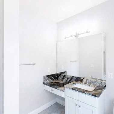 Bathroom with white cabinets, dark granite countertop, large mirror, and silver fixtures.