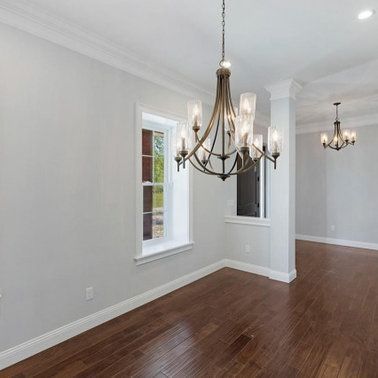 Empty room with dark hardwood floors, two chandeliers, and a window.