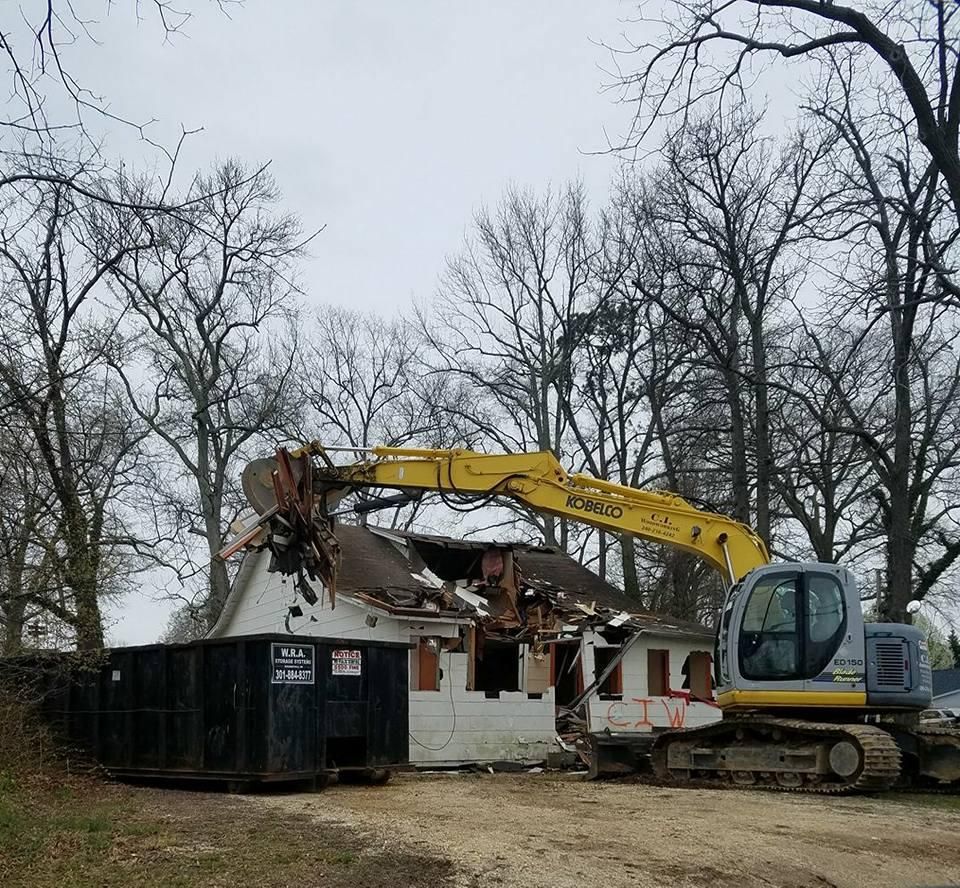 A house is being demolished by a yellow excavator.