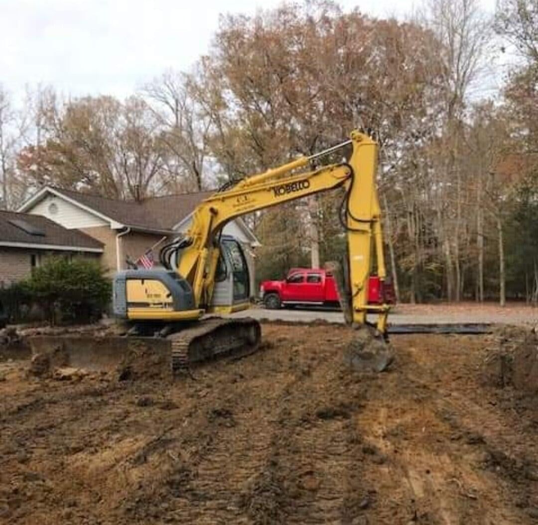 A yellow excavator is digging a hole in the dirt in front of a house.