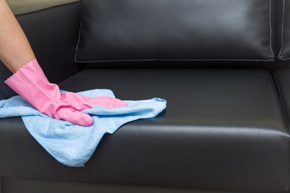 Hand in Pink Glove Wipes a Black Leather Couch With a Blue Cloth — Cairns Local Cleaning Services in Woree, QLD