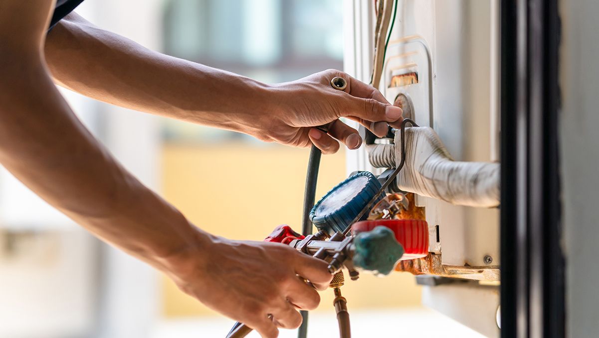 Two beige generators with black panels and cables on a gravel surface near a fence.