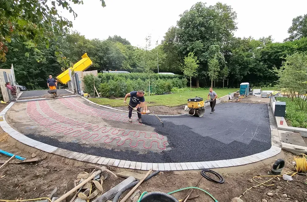 Workers in an orange vest installing large blue pipes in a trench, surrounded by debris.