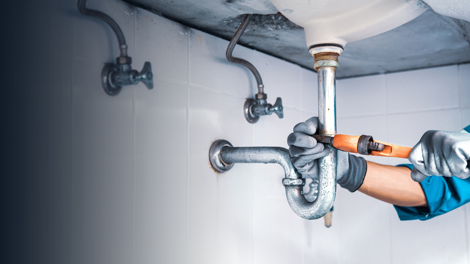 Plumber repairing sink drain with wrench, in a bathroom, wearing gloves.