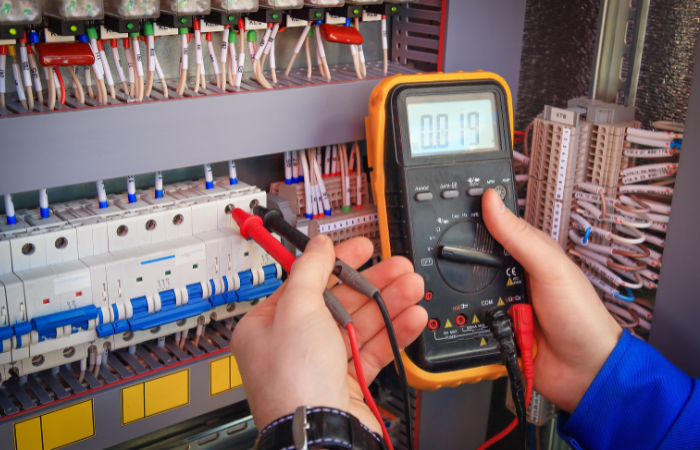 Electrician using a multimeter to test wiring in a control panel.
