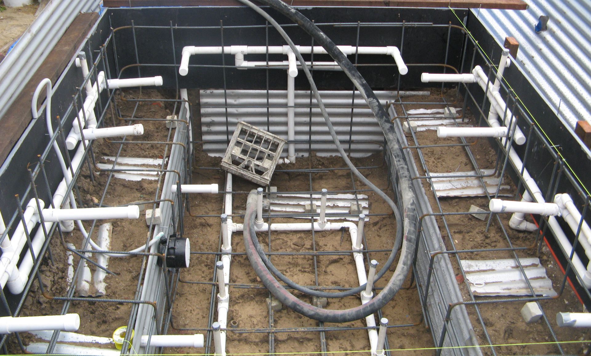 Driveway construction: red radiant heating tubes laid on wire mesh in front of a large house with a gray roof.