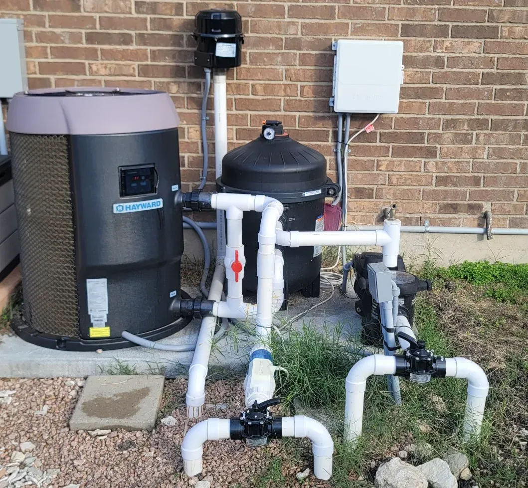 Two beige generators with black panels and cables on a gravel surface near a fence.