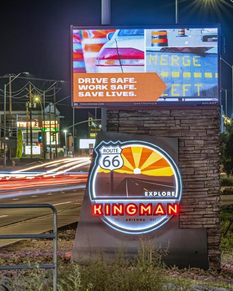 Kingman, Arizona welcome sign. Lit Route 66 emblem with digital sign urging safe driving. Night setting.