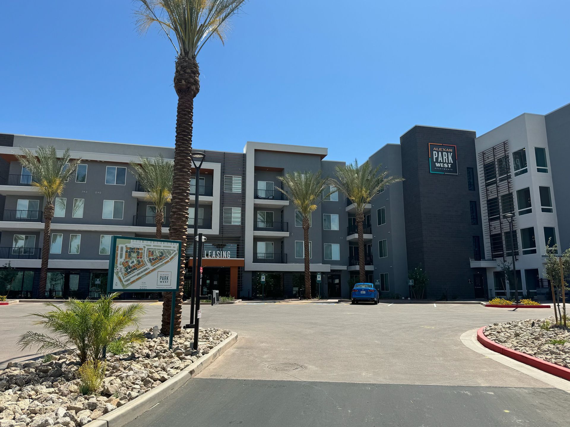 Modern, multi-story apartment building with palm trees under a clear blue sky.