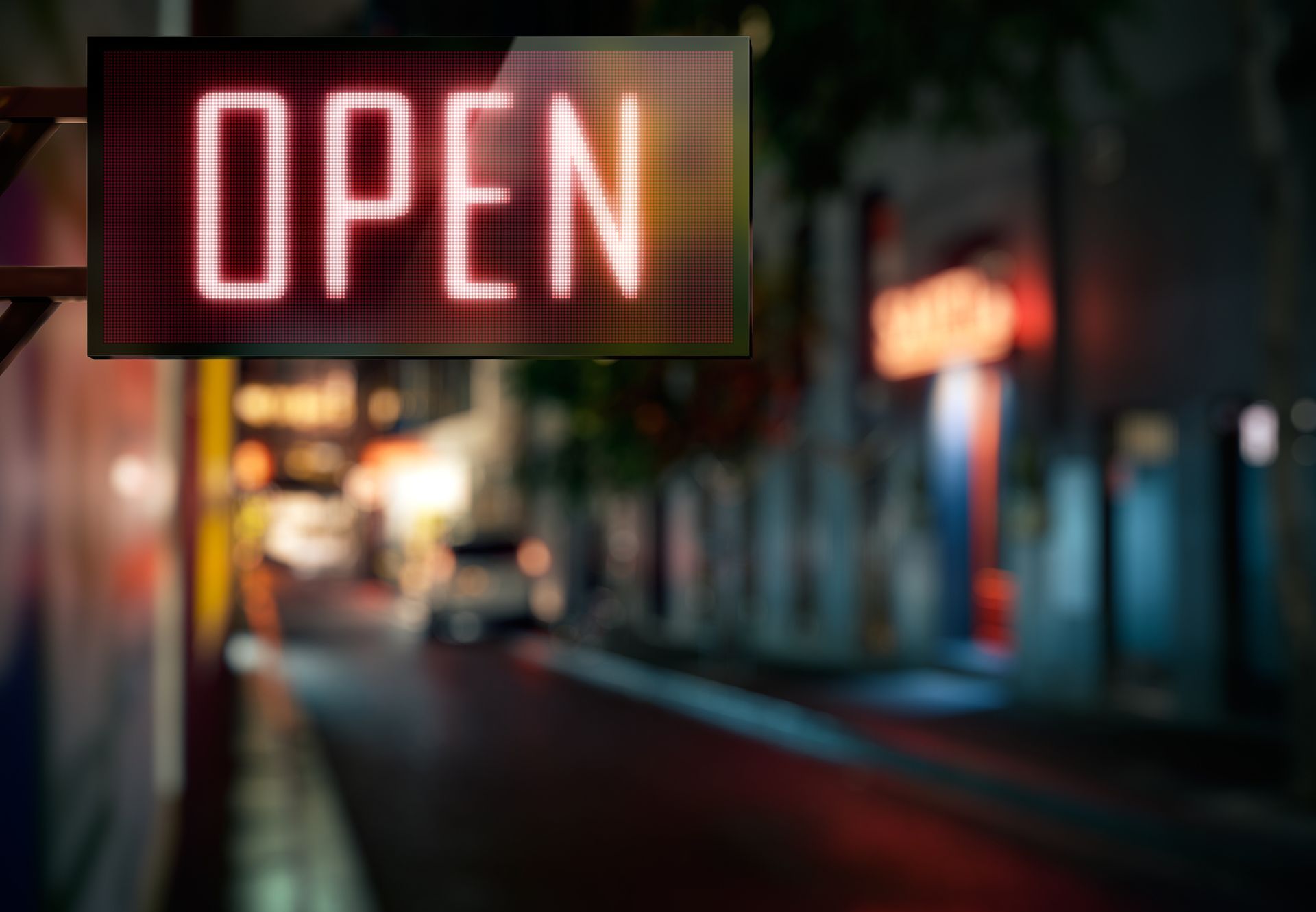 A digital 'open' sign glowing on a city street at night with blurred lights in the background