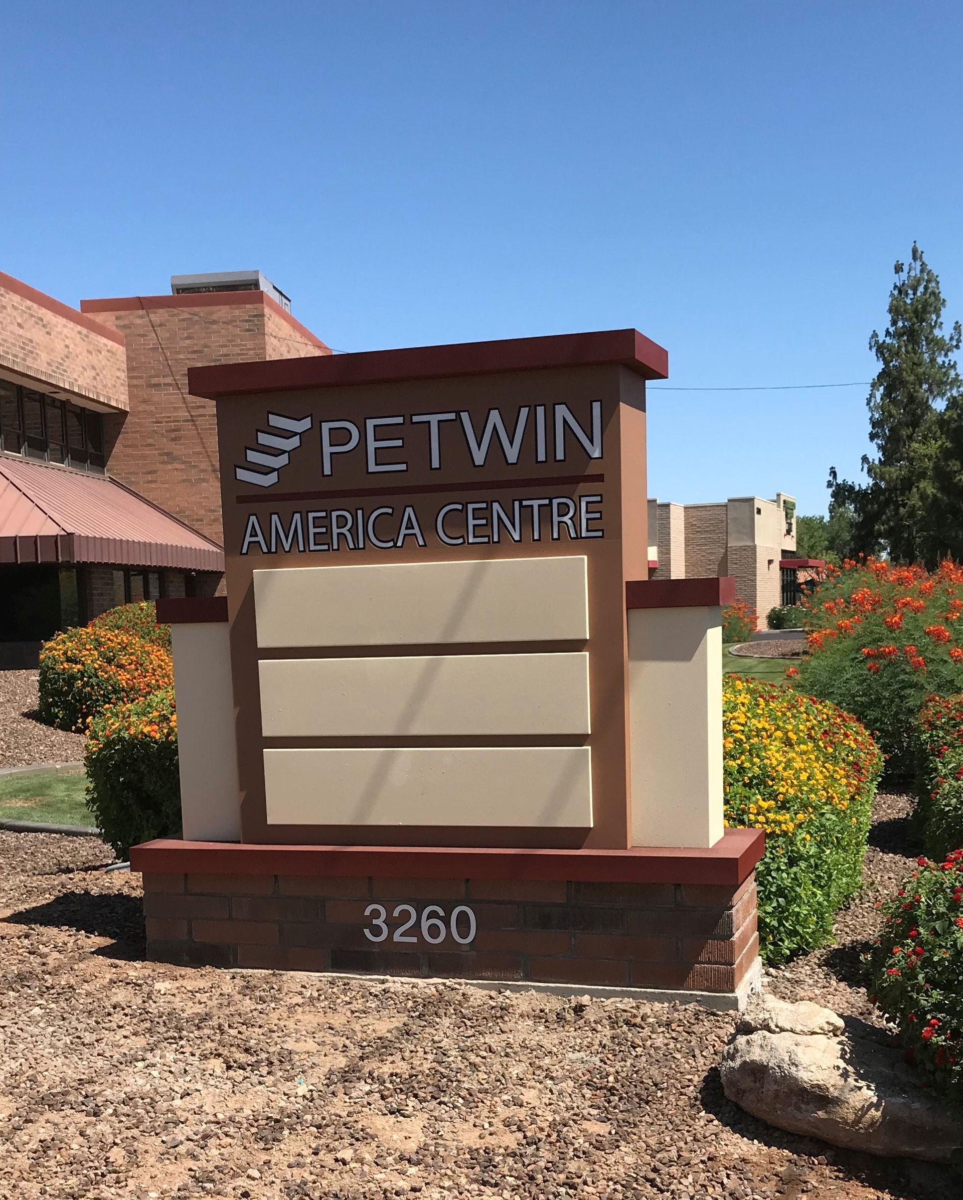 Sign for Petwin America Centre, brown and tan, in front of a building and landscaping, blue sky, 3260 address.