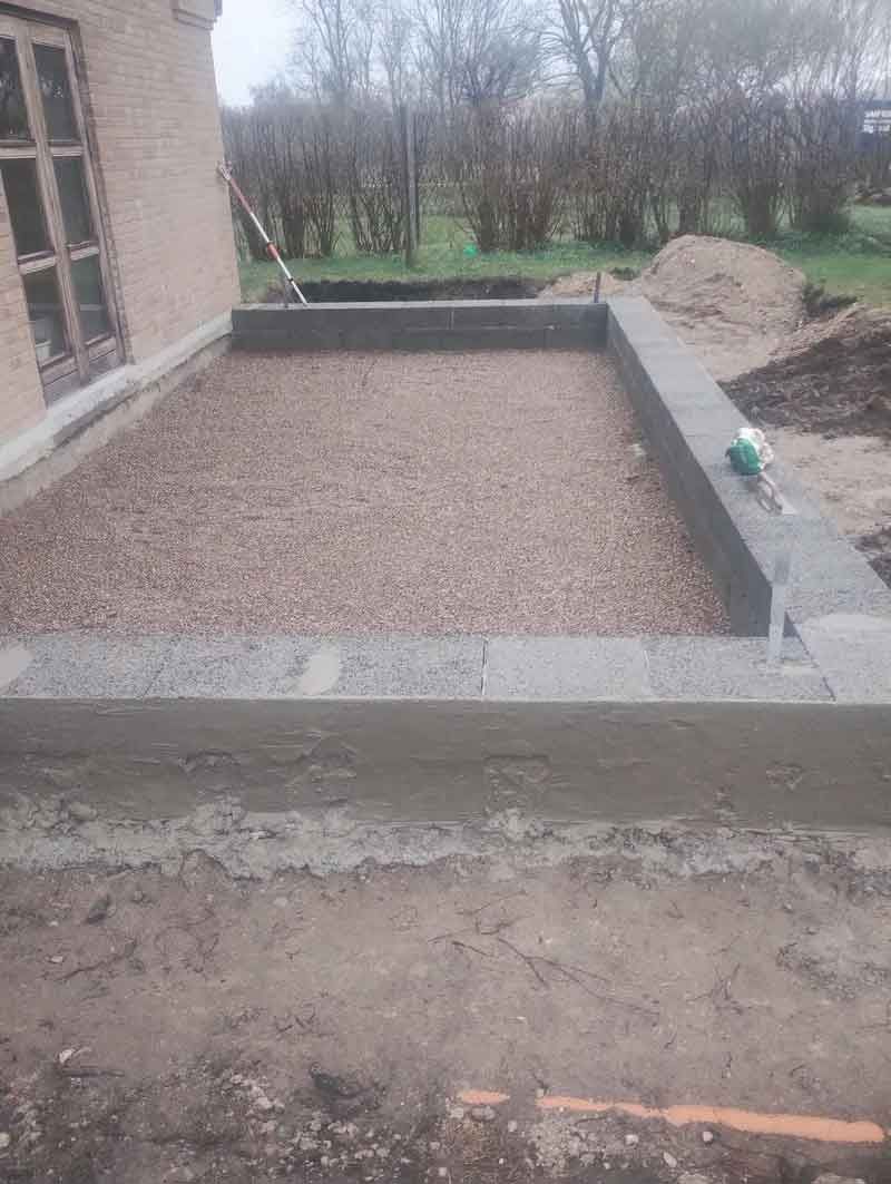 Der bygges et betonfundament foran en murstensbygning.