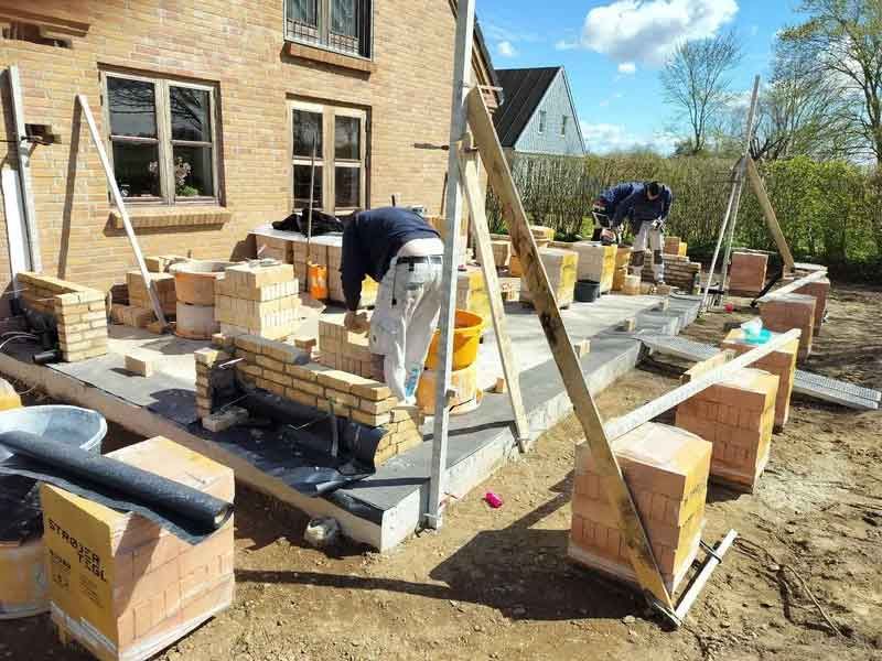 En mand arbejder på en mur foran et hus.