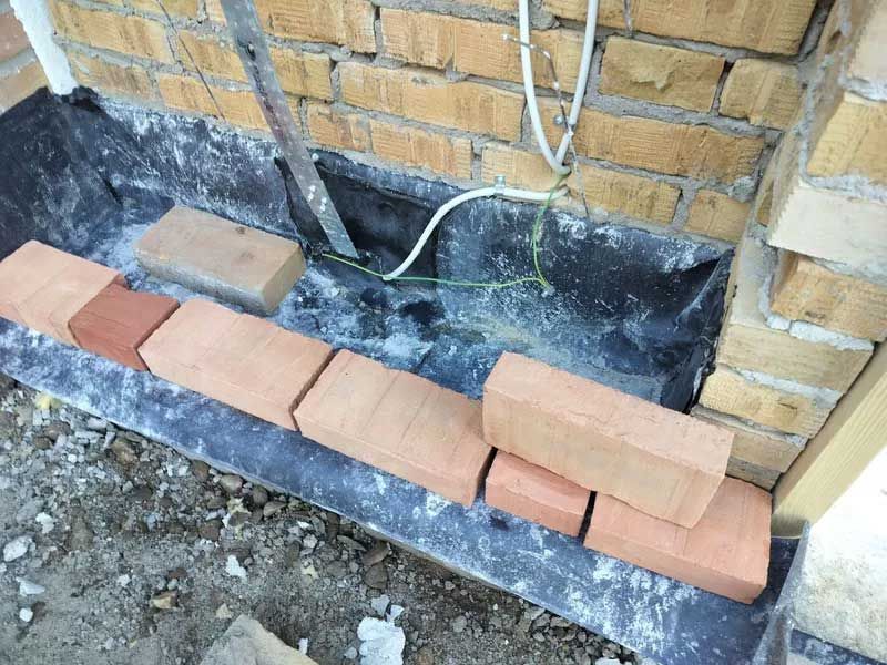 En flok mursten sidder på jorden ved siden af ​​en murstensvæg.