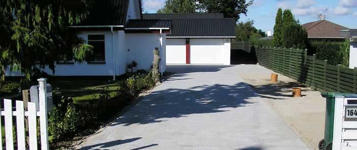 En indkørsel, der fører til et hvidt hus med sort tag