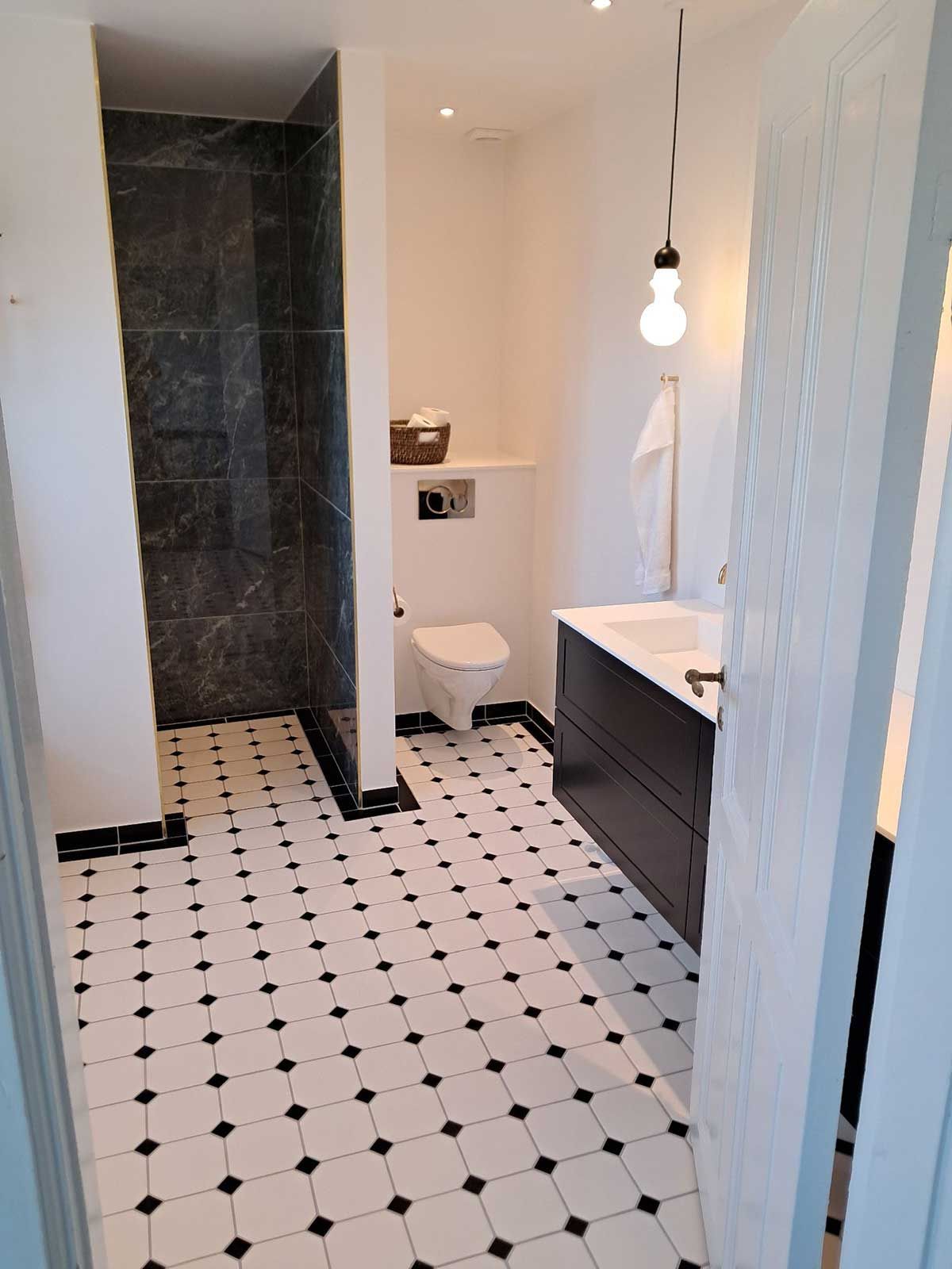 Et badeværelse med sorte og hvide klinker og et toilet