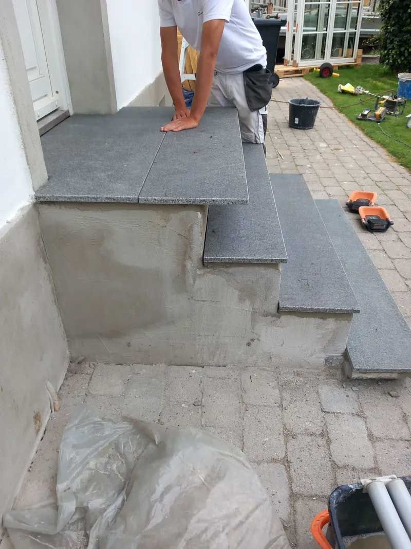 En mand lægger fliser på trappen til et hus.