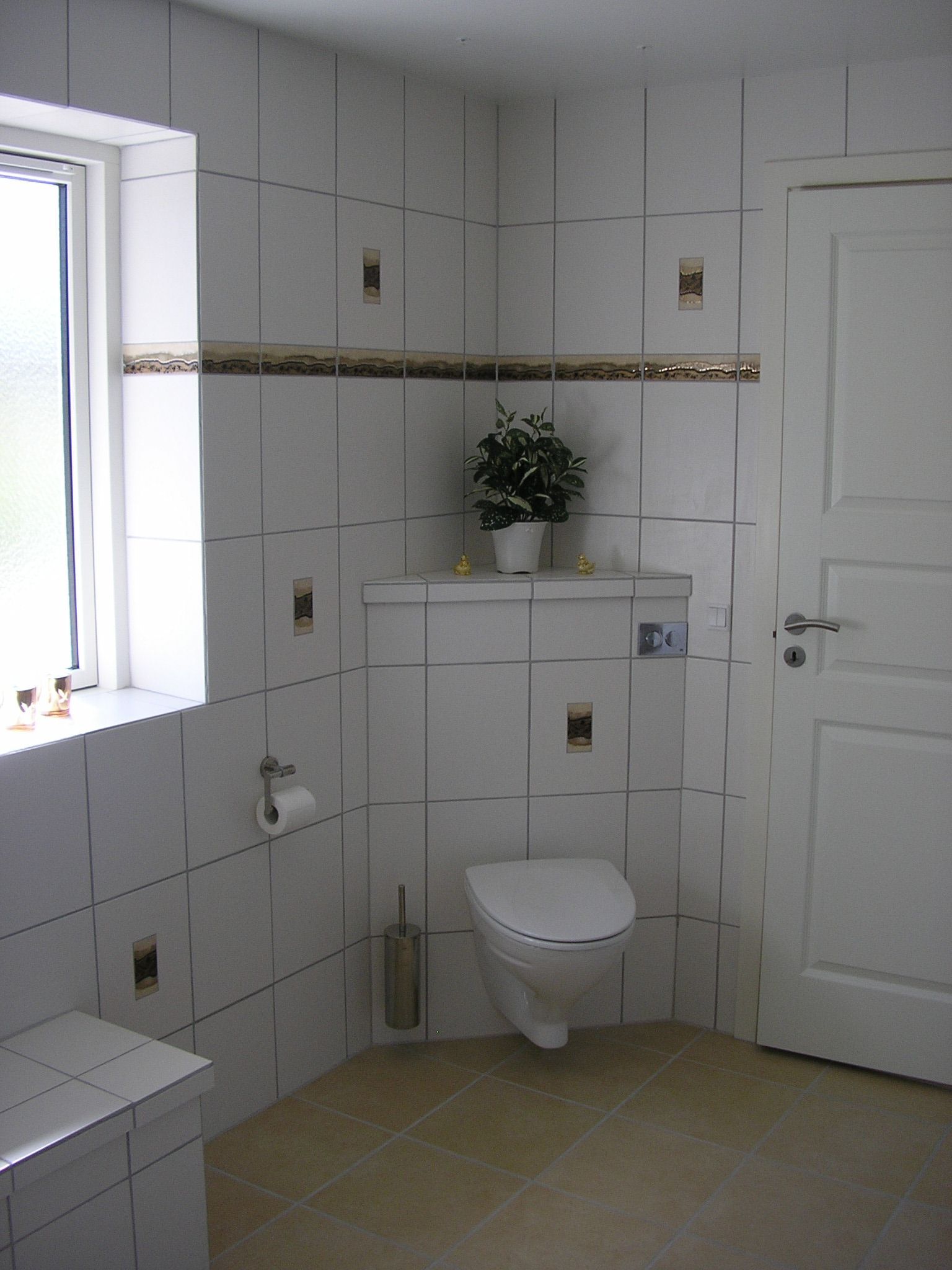 Et badeværelse med hvide klinker og et toilet