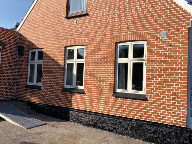 Et rødt murstenshus med hvide vinduer og en rampe.