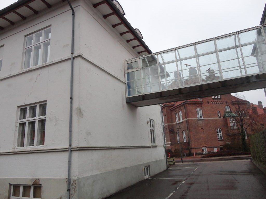 En hvid bygning med en glasgang mellem sig og en anden bygning