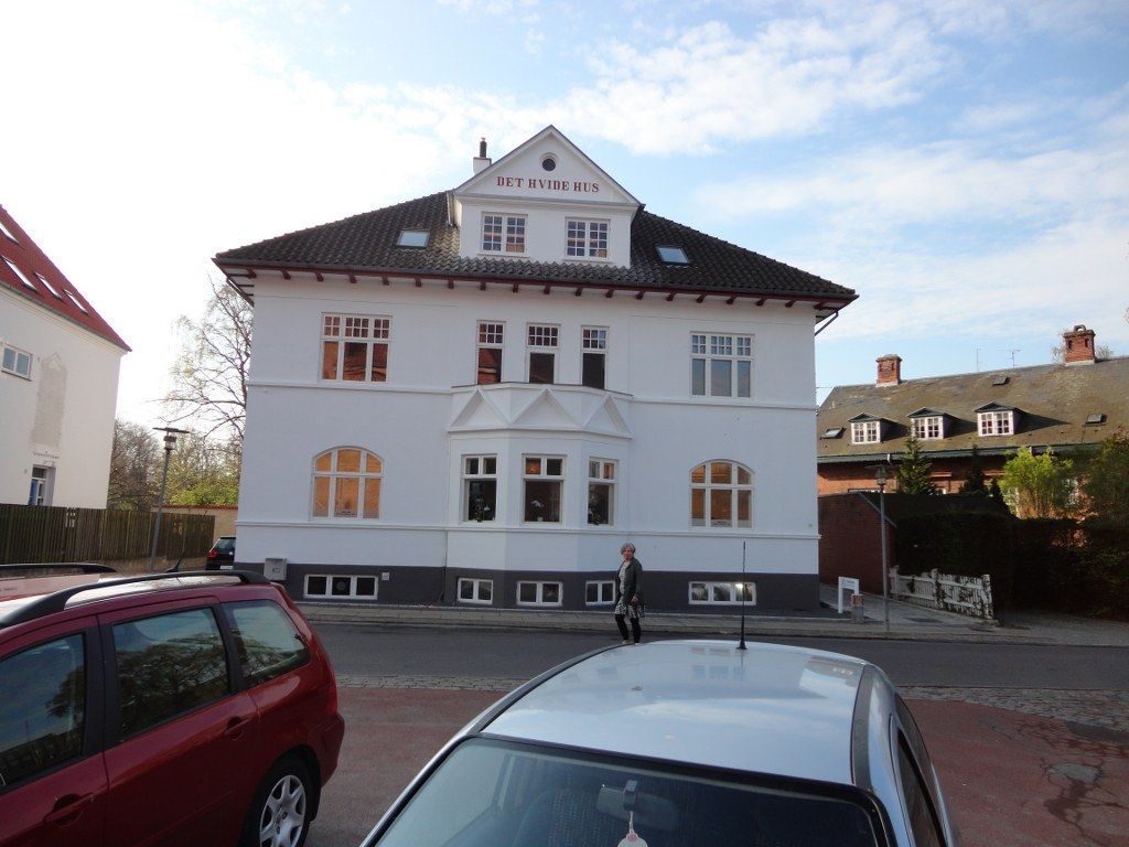 En hvid bygning med sort tag og en hvid bil parkeret foran