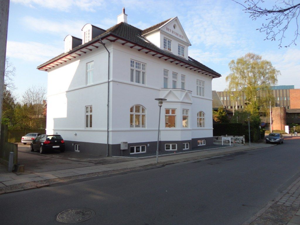 En stor hvid bygning med biler parkeret foran