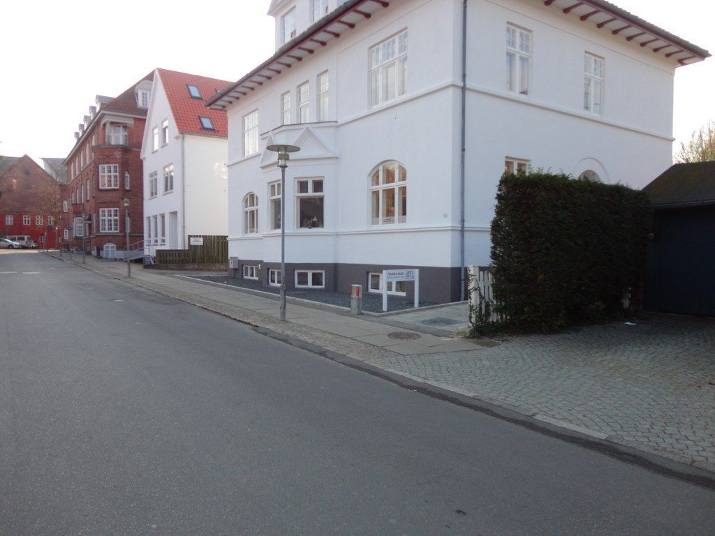 En hvid bygning med rødt tag ligger på siden af ​​en gade