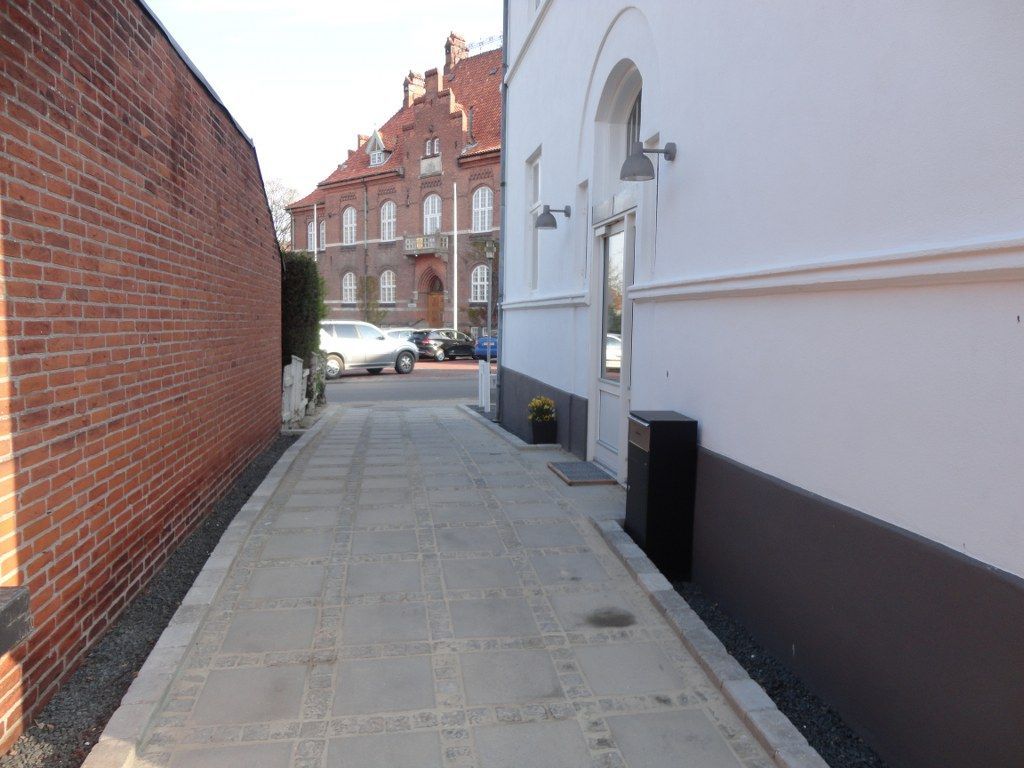 En smal gyde mellem to bygninger med biler parkeret i baggrunden