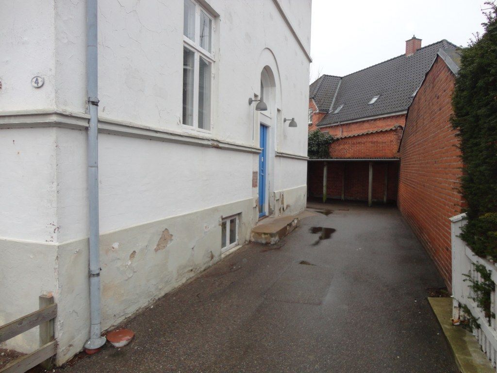 En hvid bygning med en blå dør ligger ved siden af ​​en murstensbygning