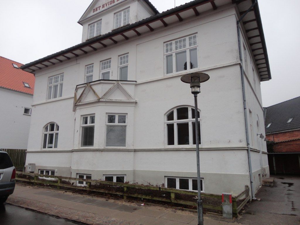 En stor hvid bygning med en bil parkeret foran