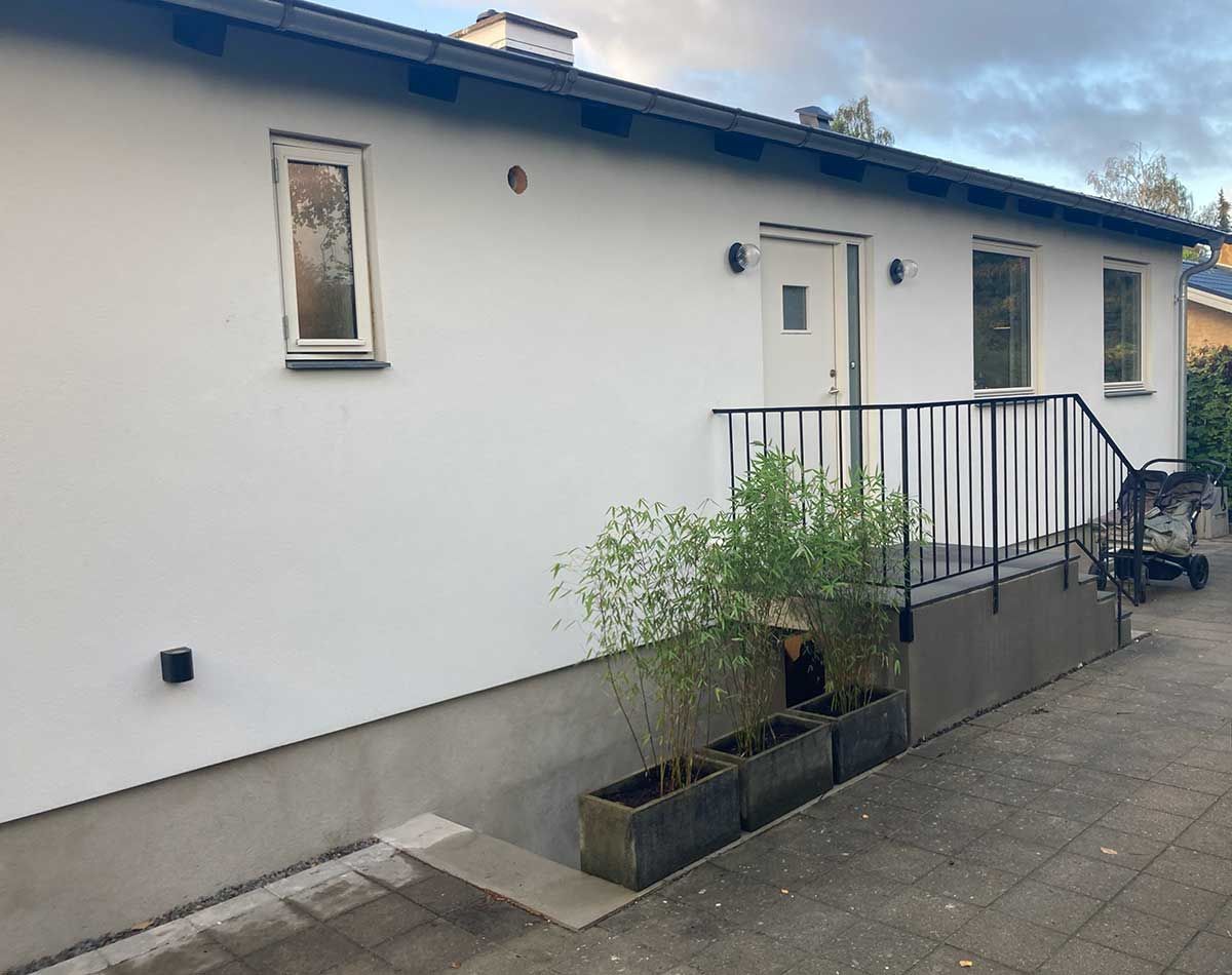 Et hvidt hus med et sort rækværk og plantekasser foran.