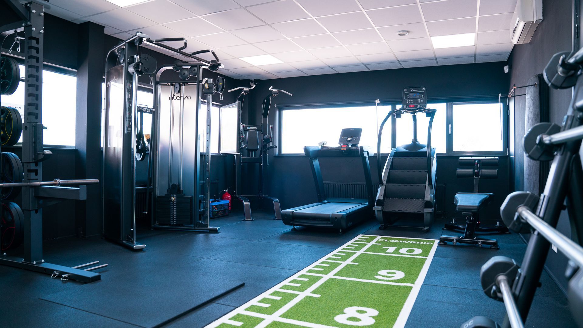 Gym with weight machines, barbells, and a treadmill on a green and black floor.