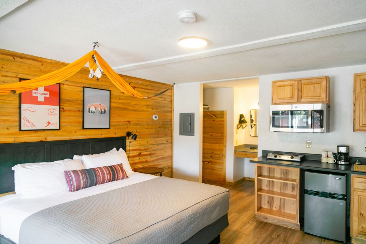 Small hotel room with a bed, wood accent wall, kitchenette, and bathroom doorway