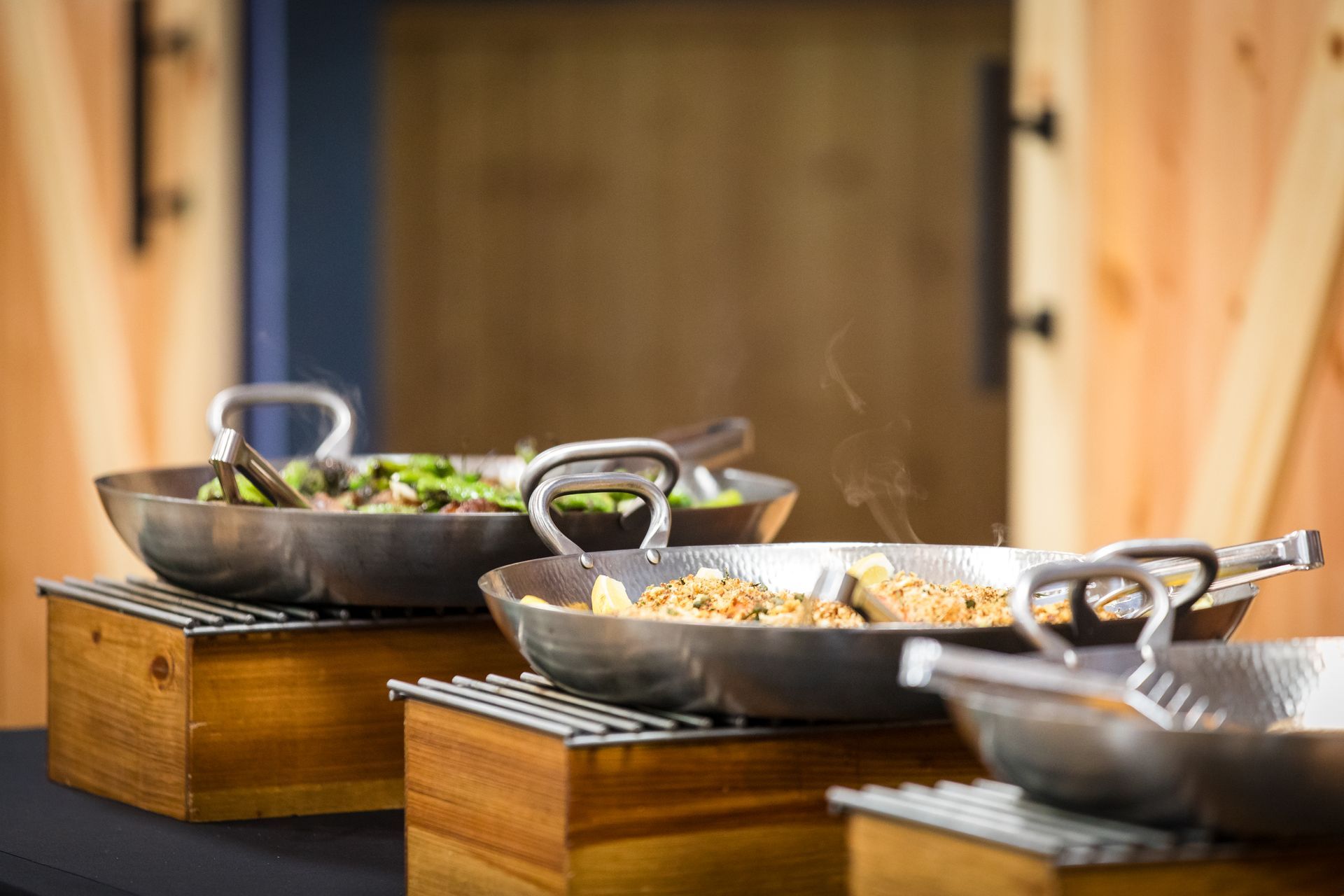 Three cast-iron serving pans on wooden risers with food in a buffet setting