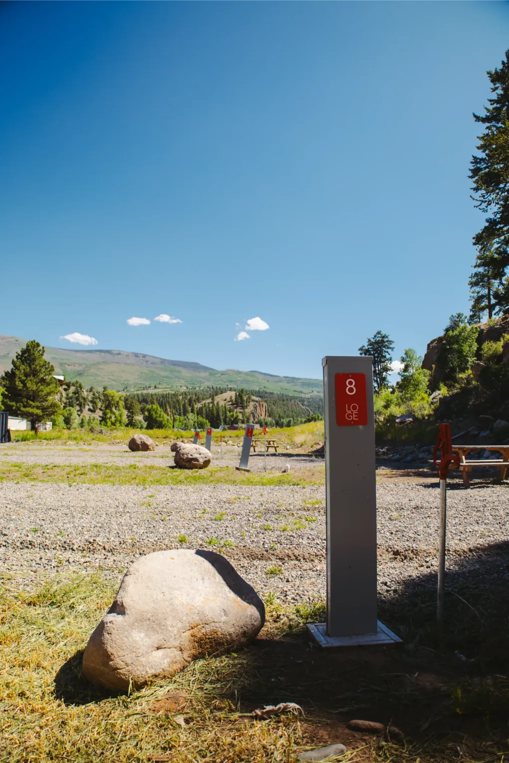 Scenic mountain overlook with gravel lot, large rock, and red signpost under a bright blue sky