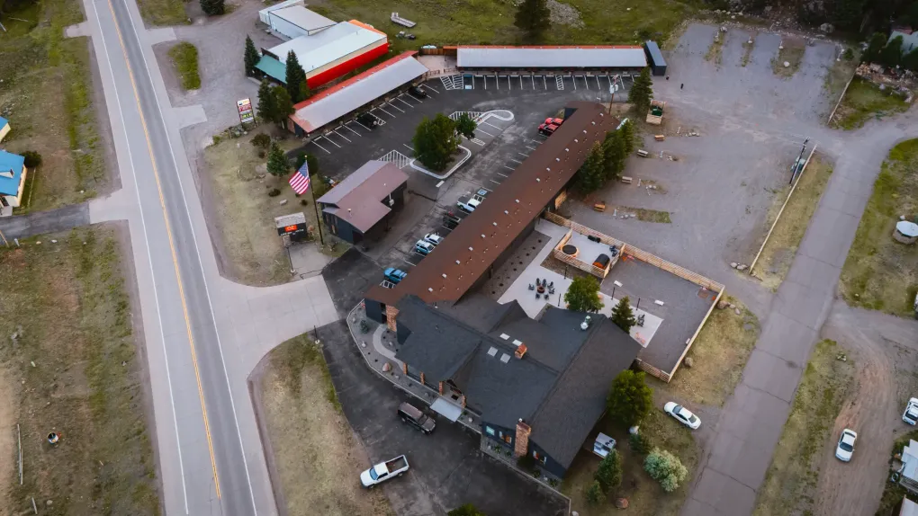 Aerial view of a roadside building with a parking lot, surrounding trees, and nearby vehicles.