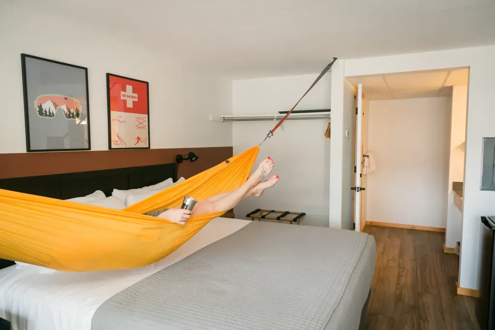 Person resting in a yellow hammock beside a bed in a bright bedroom