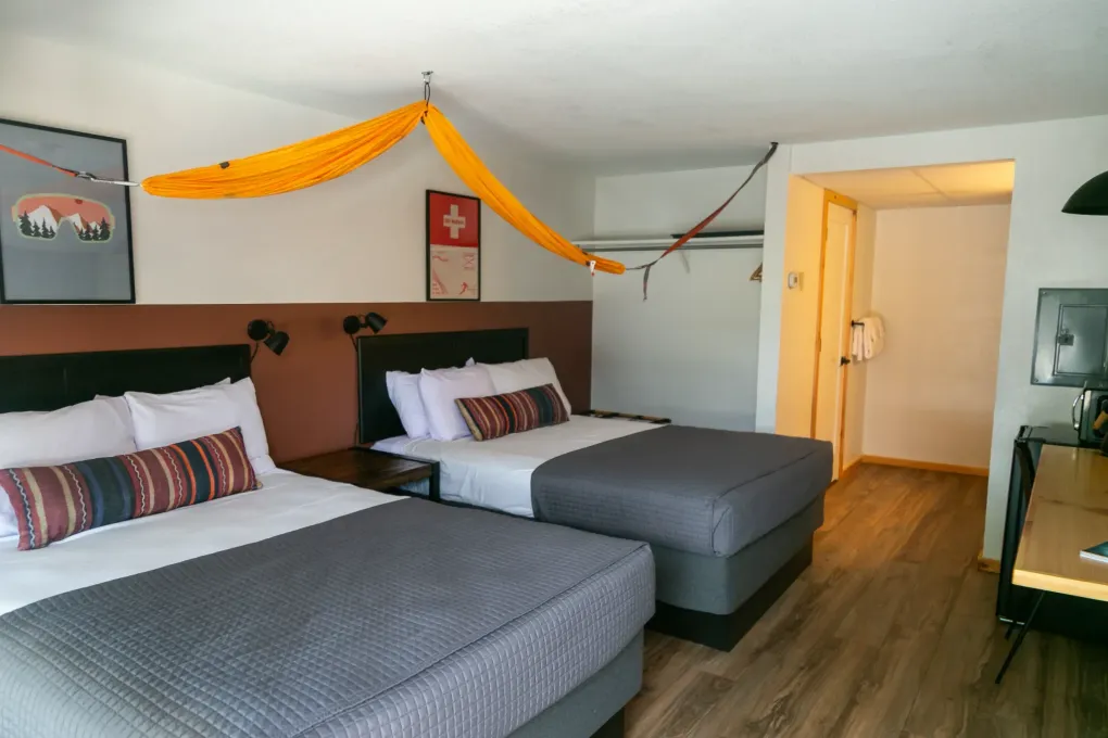 Hotel room with two gray beds, wooden floor, and orange garland across the wall.