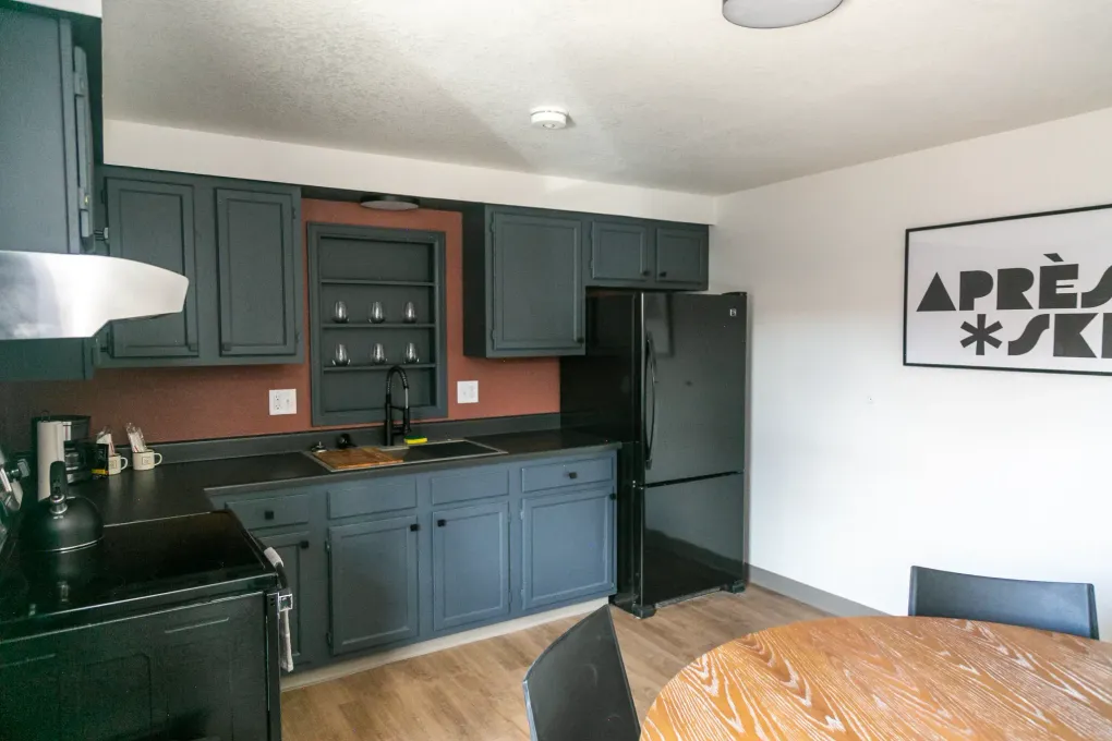 Small kitchen with dark cabinets, black appliances, and a round wooden table beside a wall art print.
