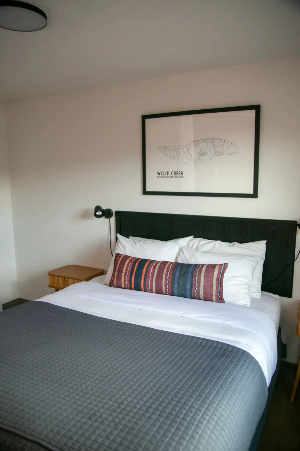 Neatly made bed with white and gray bedding in a minimalist bedroom, with framed art above the headboard