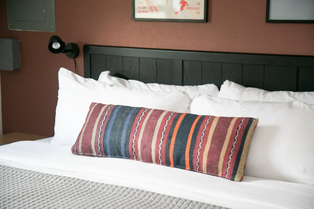 Neatly made bed with white pillows and a colorful striped lumbar pillow against a dark headboard.