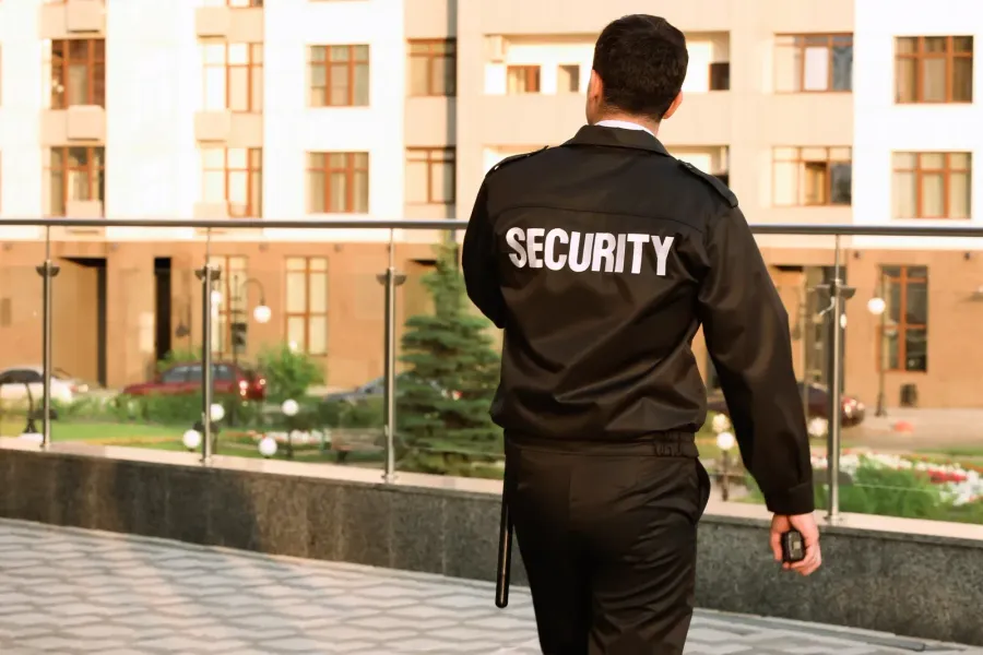 A security guard with an APS patch on their sleeve looks out over a blurred, crowded outdoor event.
