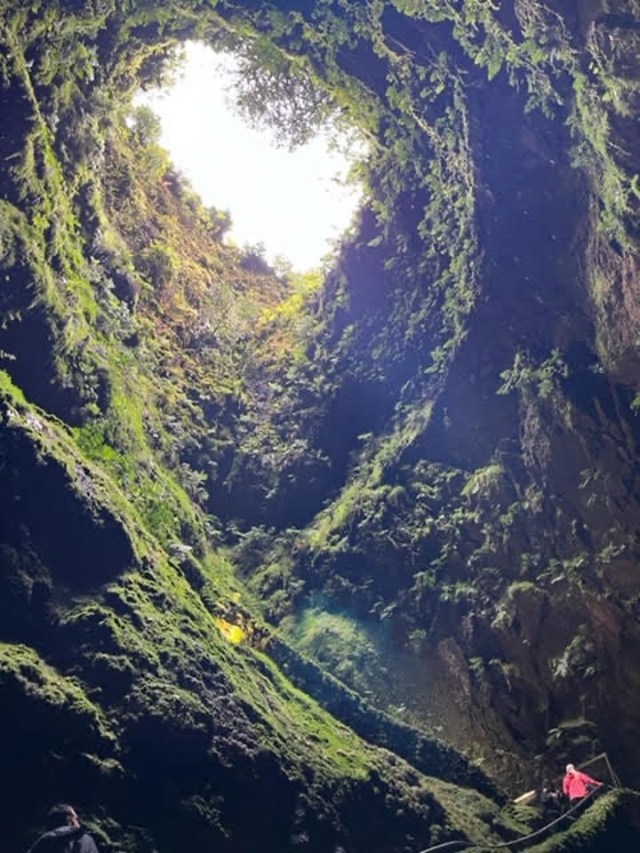 a group of people are standing in a cave looking up at the sky .