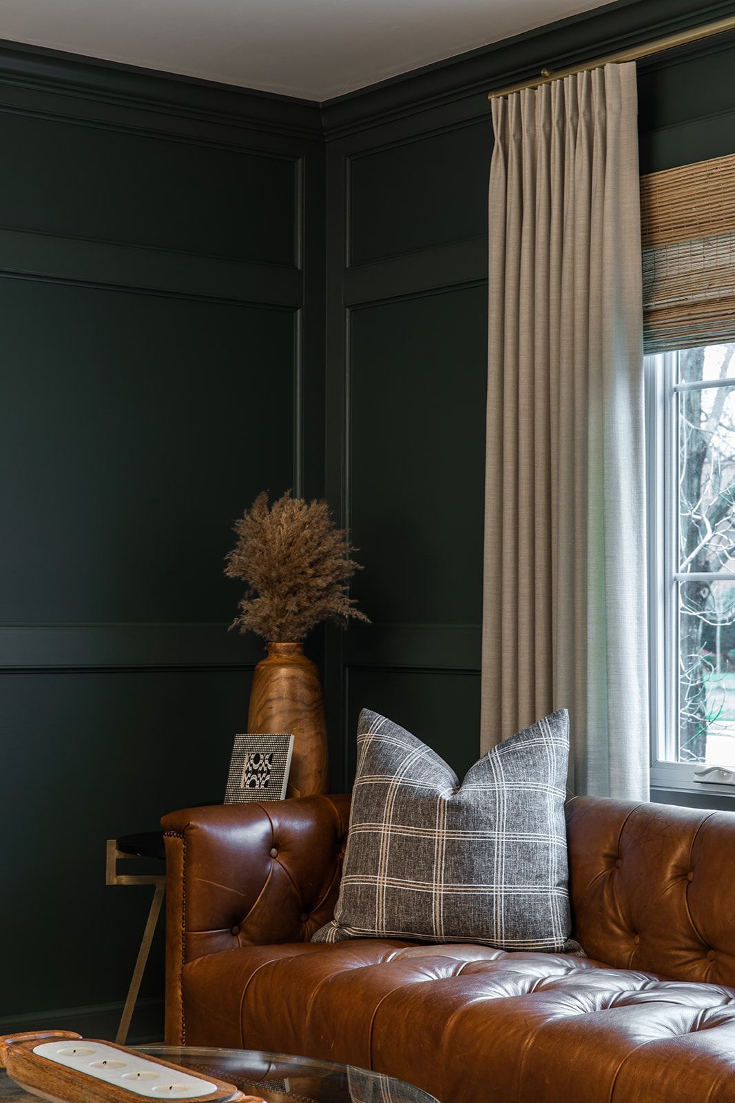 A living room with a brown leather couch and a vase of dried flowers