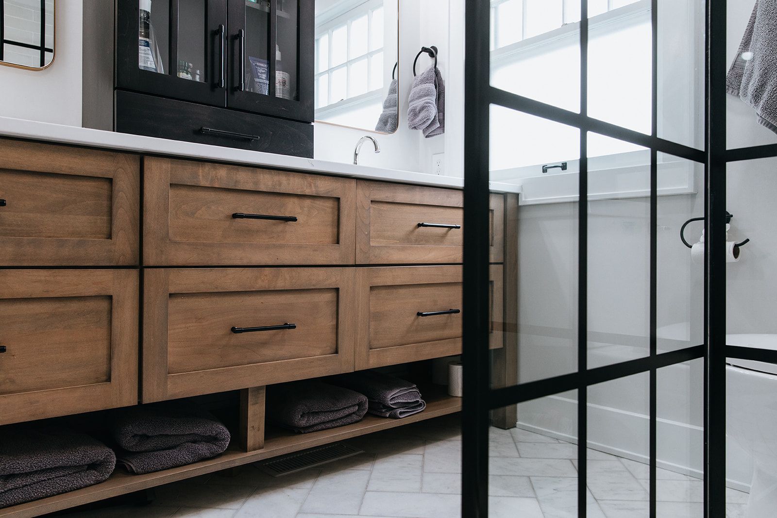 A bathroom with a glass shower door and wooden cabinets