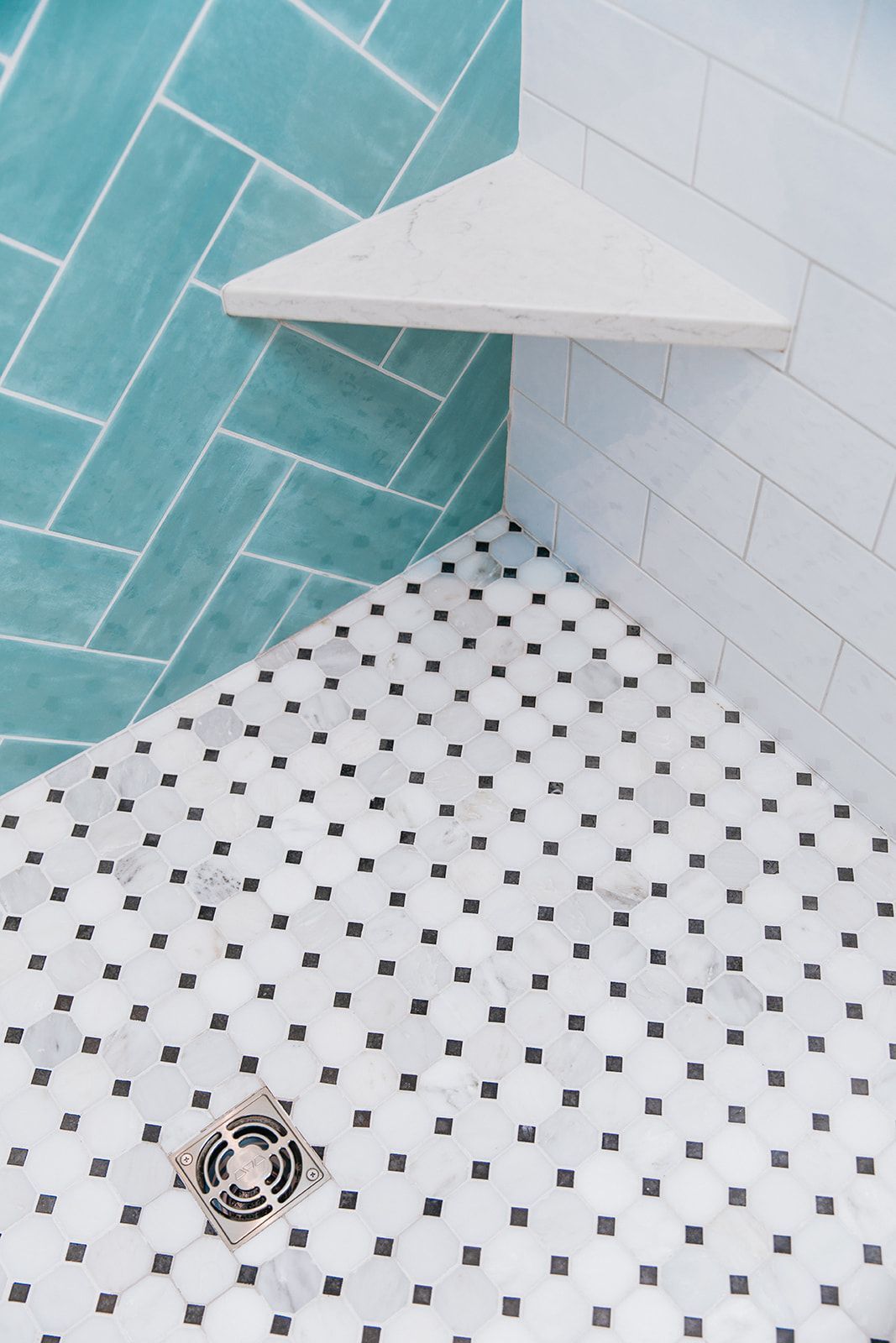 A shower with a black and white tile floor and a corner shelf