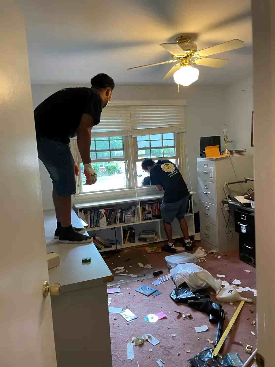 two men are working in a messy room with a ceiling fan