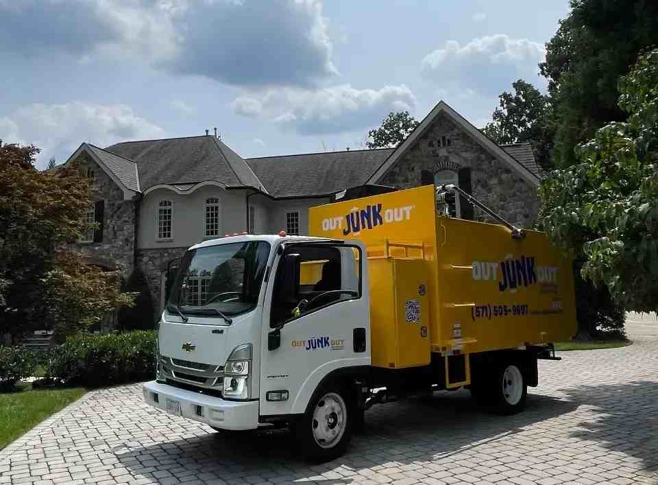 a yellow junk out truck is parked in front of a large house