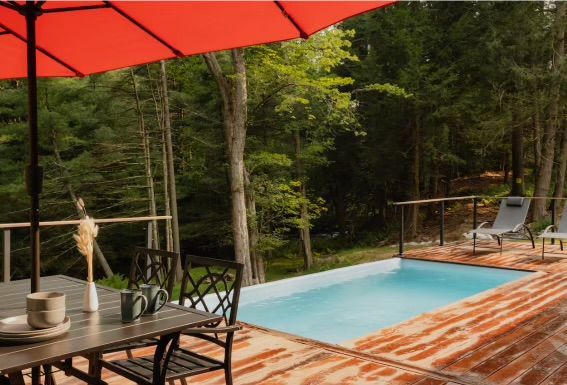 A red umbrella is sitting on a wooden deck next to a swimming pool.