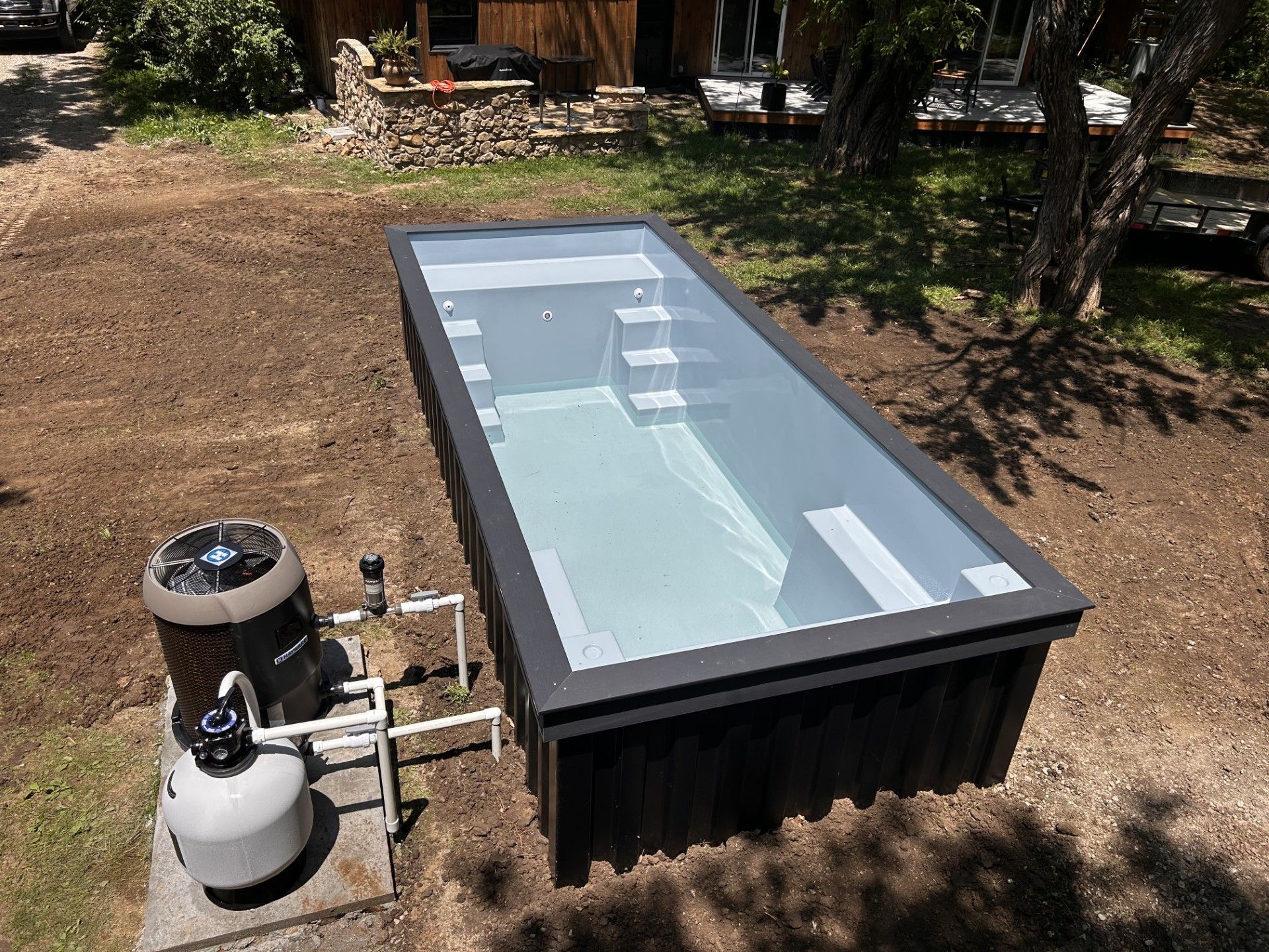 A red umbrella is sitting on a wooden deck next to a swimming pool.